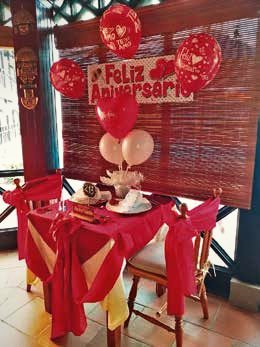 Mesa vestida en rojo con globos y cartel de Feliz Aniversario.