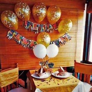 Decoración de cumpleaños con globos dorados y blancos sobre una mesa servida.
