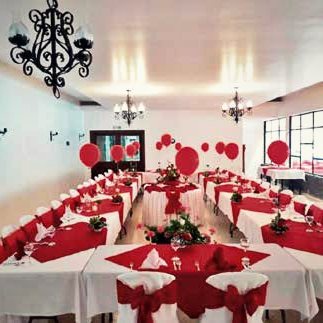 Mesa larga vestida en rojo y blanco con globos, bajo arañas de luz.